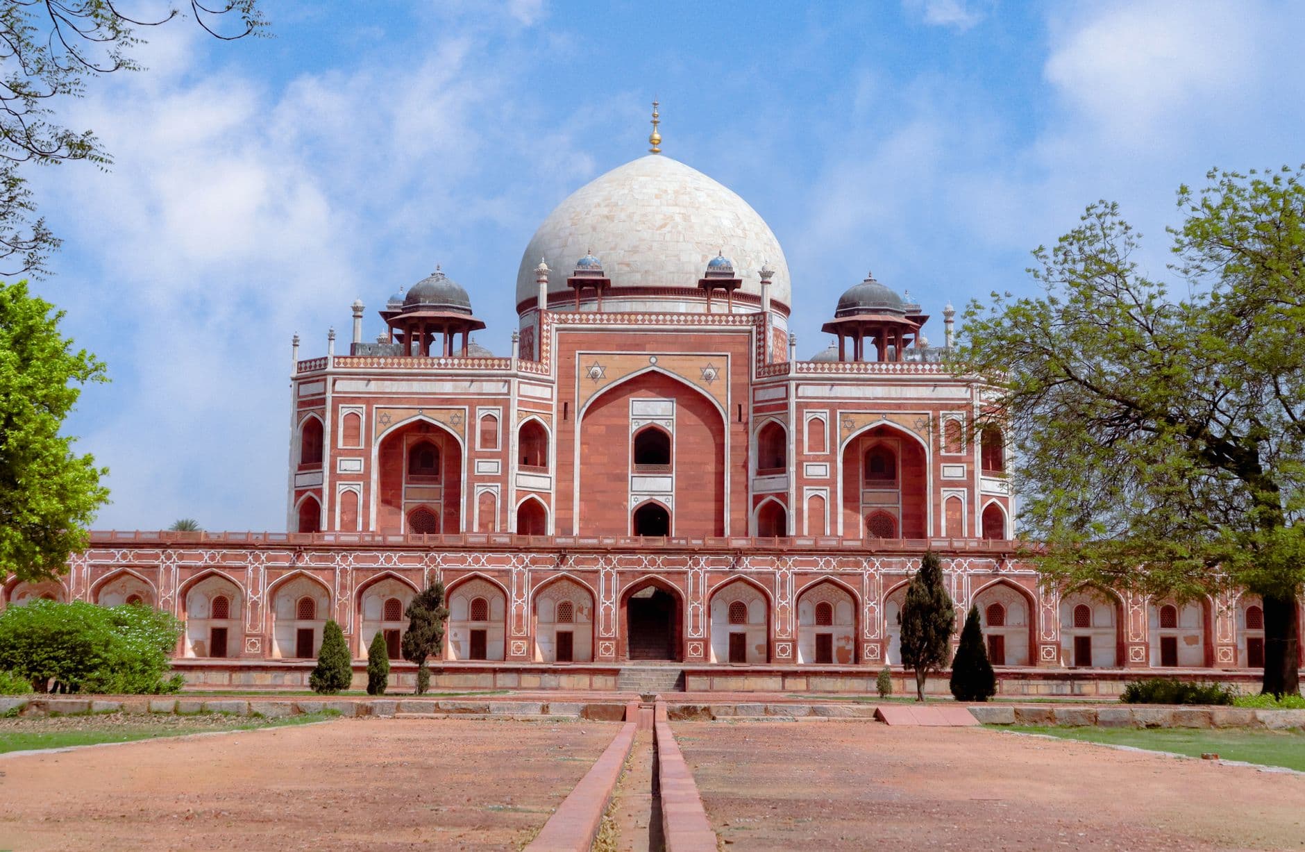 The red-and-white front facade of Humayun's Tomb under its white marble dome, seen down the charbagh garden's axis