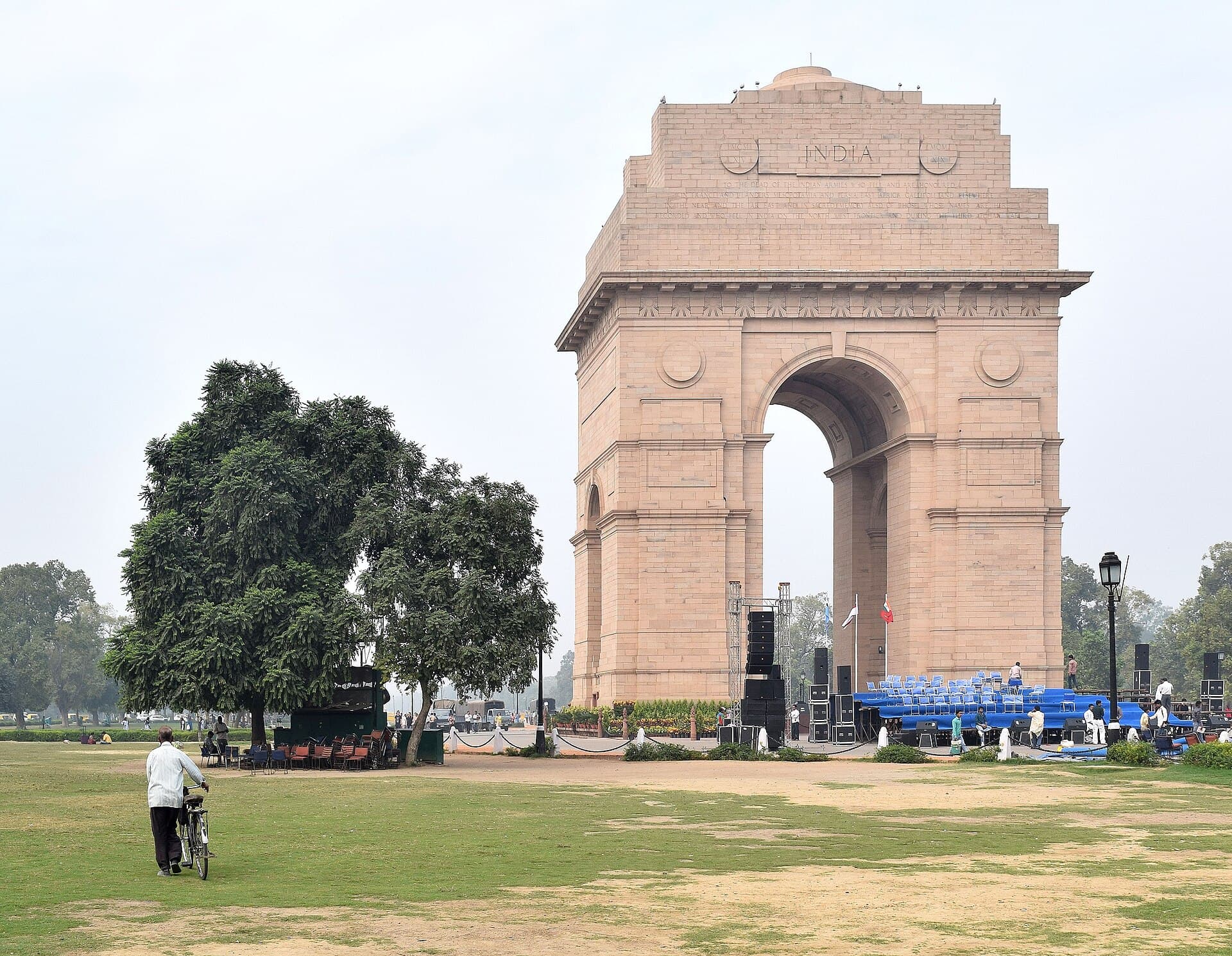 The full 42-metre arch of India Gate from the western lawns, a cyclist walking across the grass in the foreground