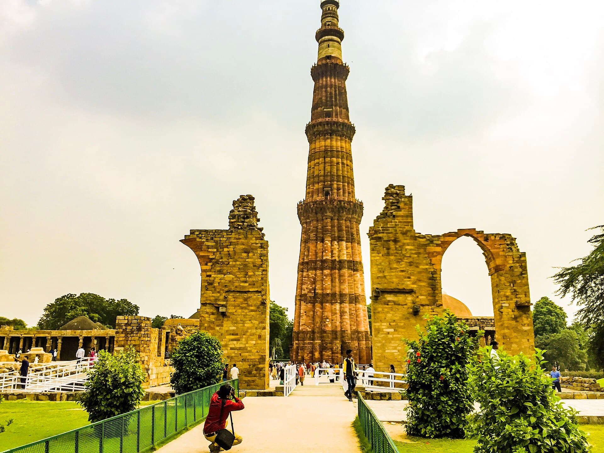The fluted sandstone shaft of Qutub Minar rising behind the ruined arches of the Quwwat-ul-Islam mosque complex