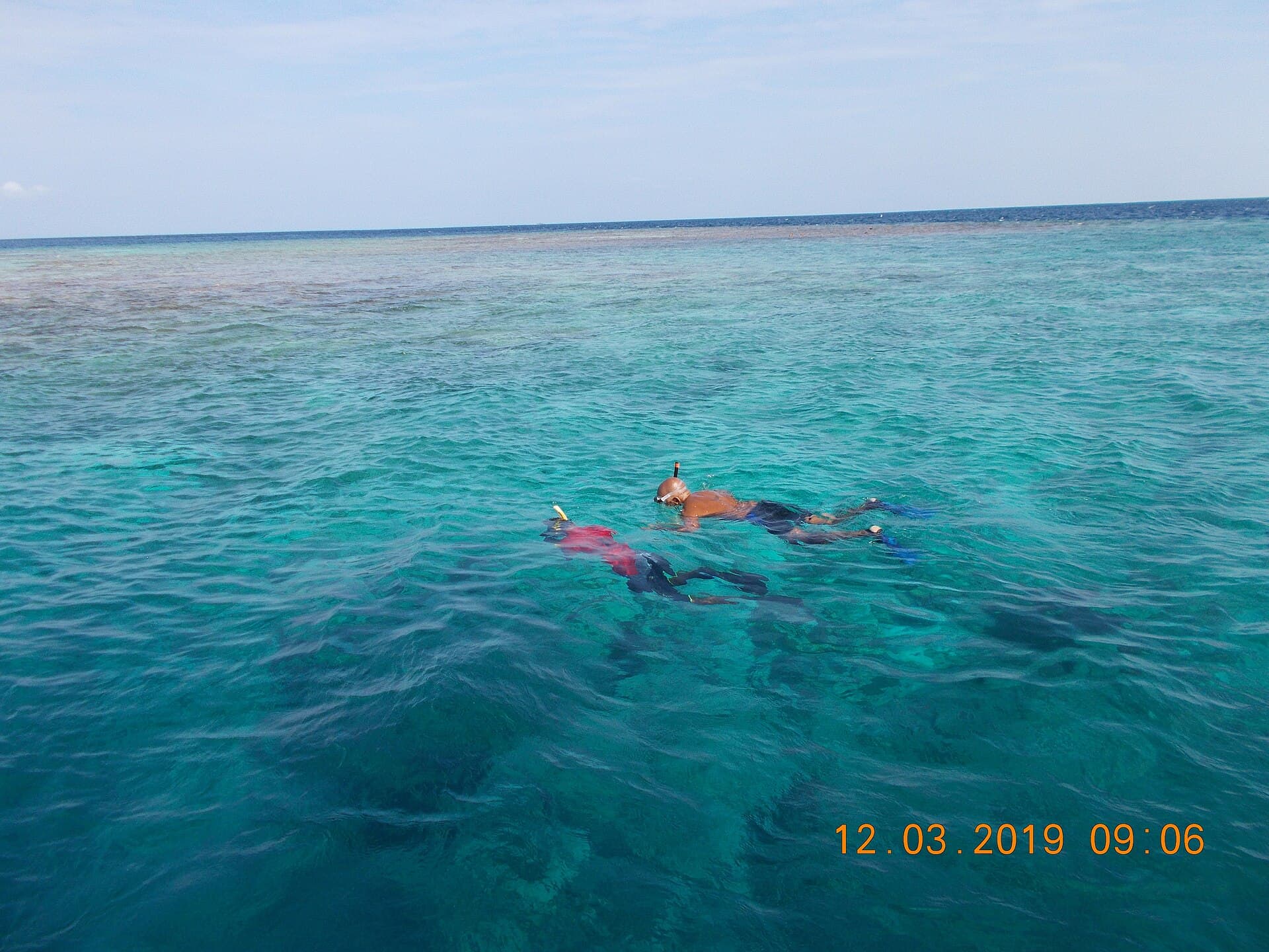 Two snorkellers swimming over a shallow reef in clear Maldivian water
