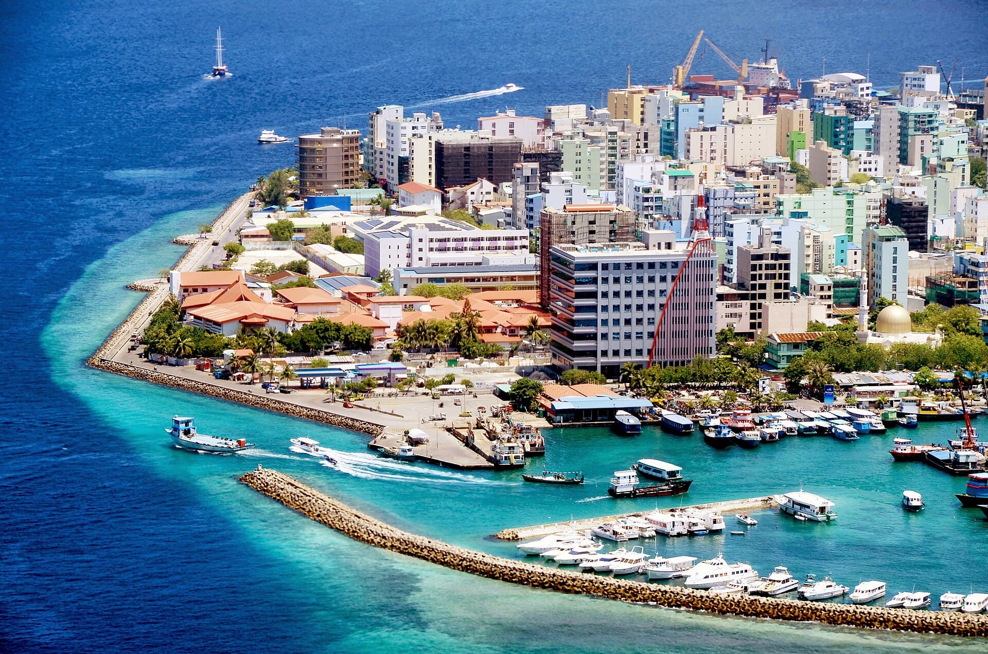 Aerial view of Malé's densely packed colourful buildings and busy harbour, with the Maldives' turquoise reef beyond