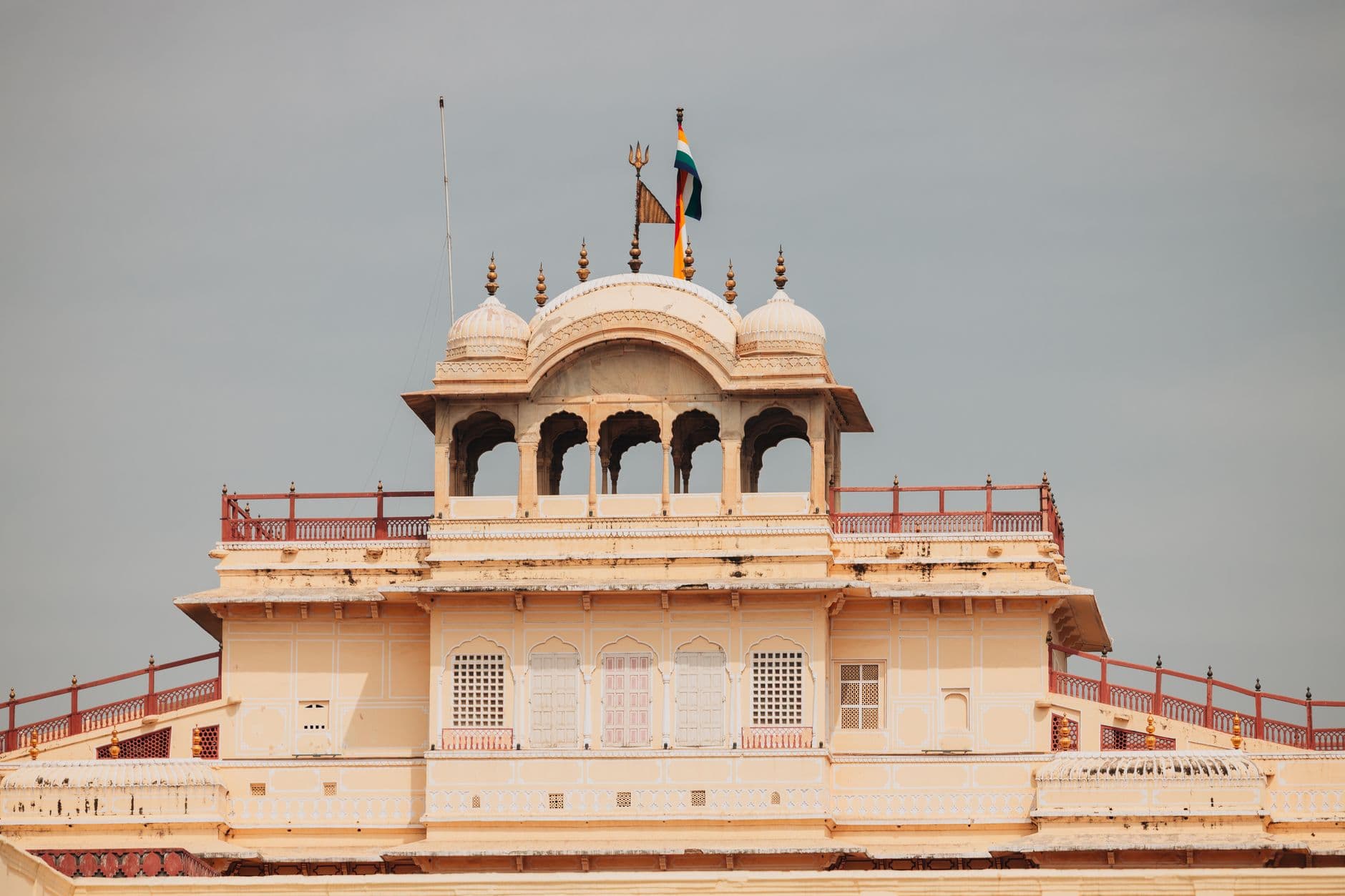 A domed rooftop pavilion of Jaipur's City Palace with the royal standard flying, cream and pink against a monsoon sky