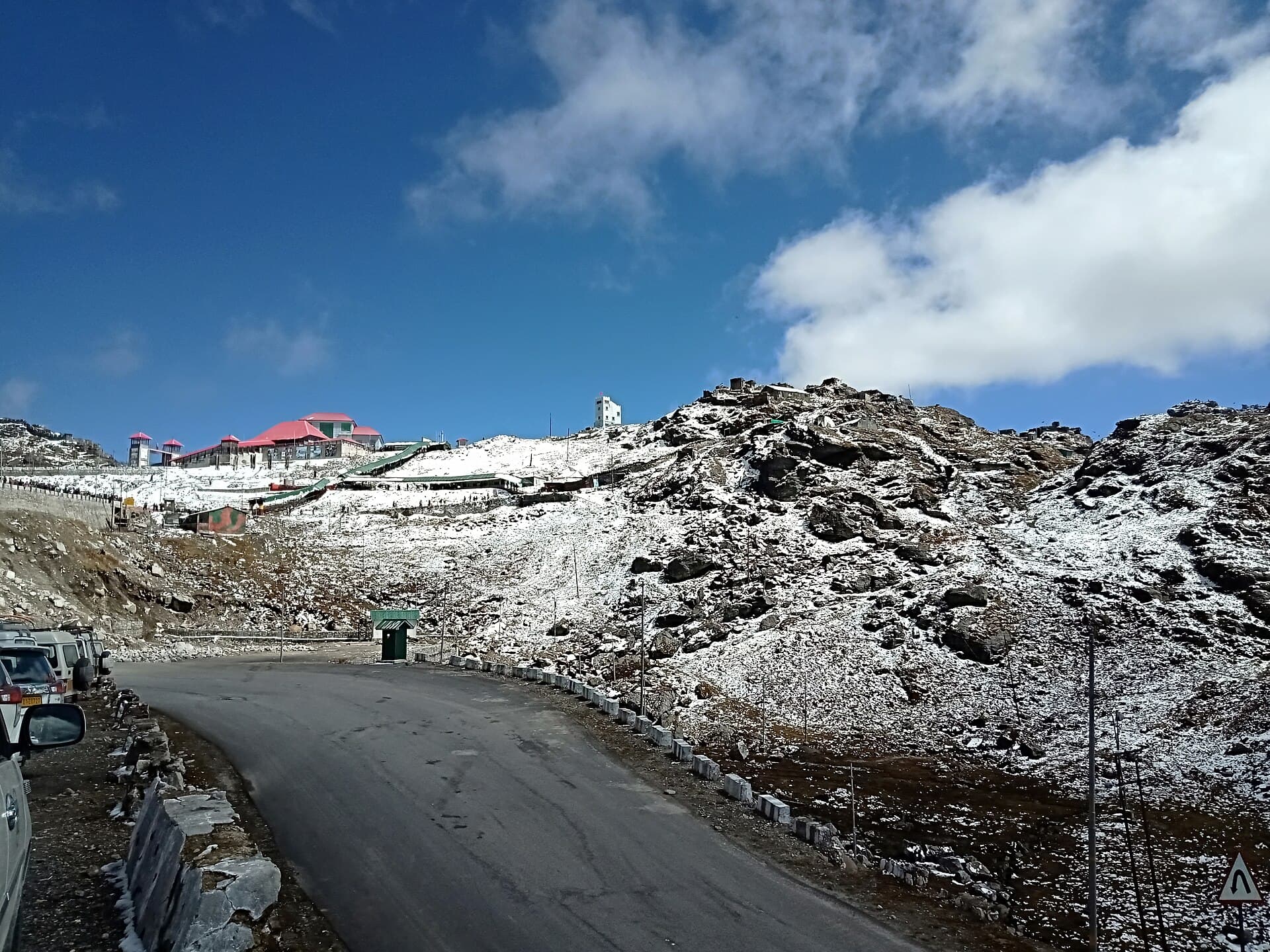 The road curving up to Nathula Pass through snow-dusted slopes, the red-roofed border complex on the ridge above