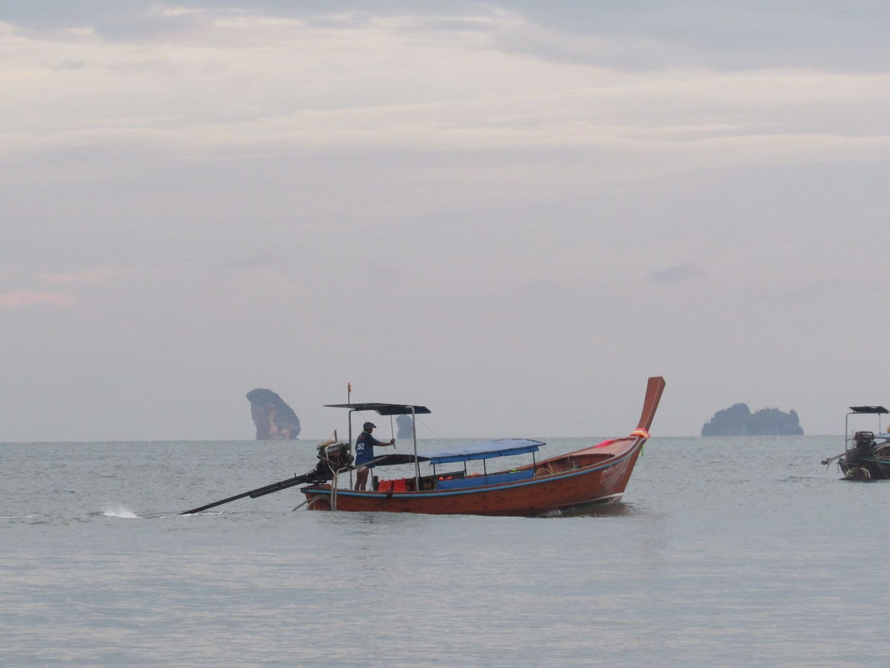 A traditional wooden longtail boat drifting on a calm Thai seascape at dusk