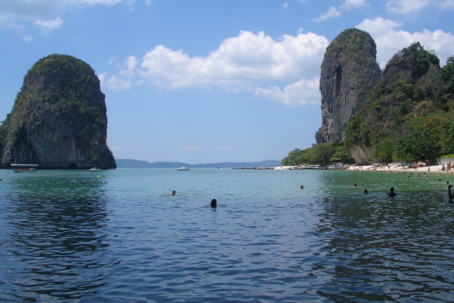 Railay's sheer limestone cliffs bracketing a turquoise bay, swimmers and longtail boats in the water below