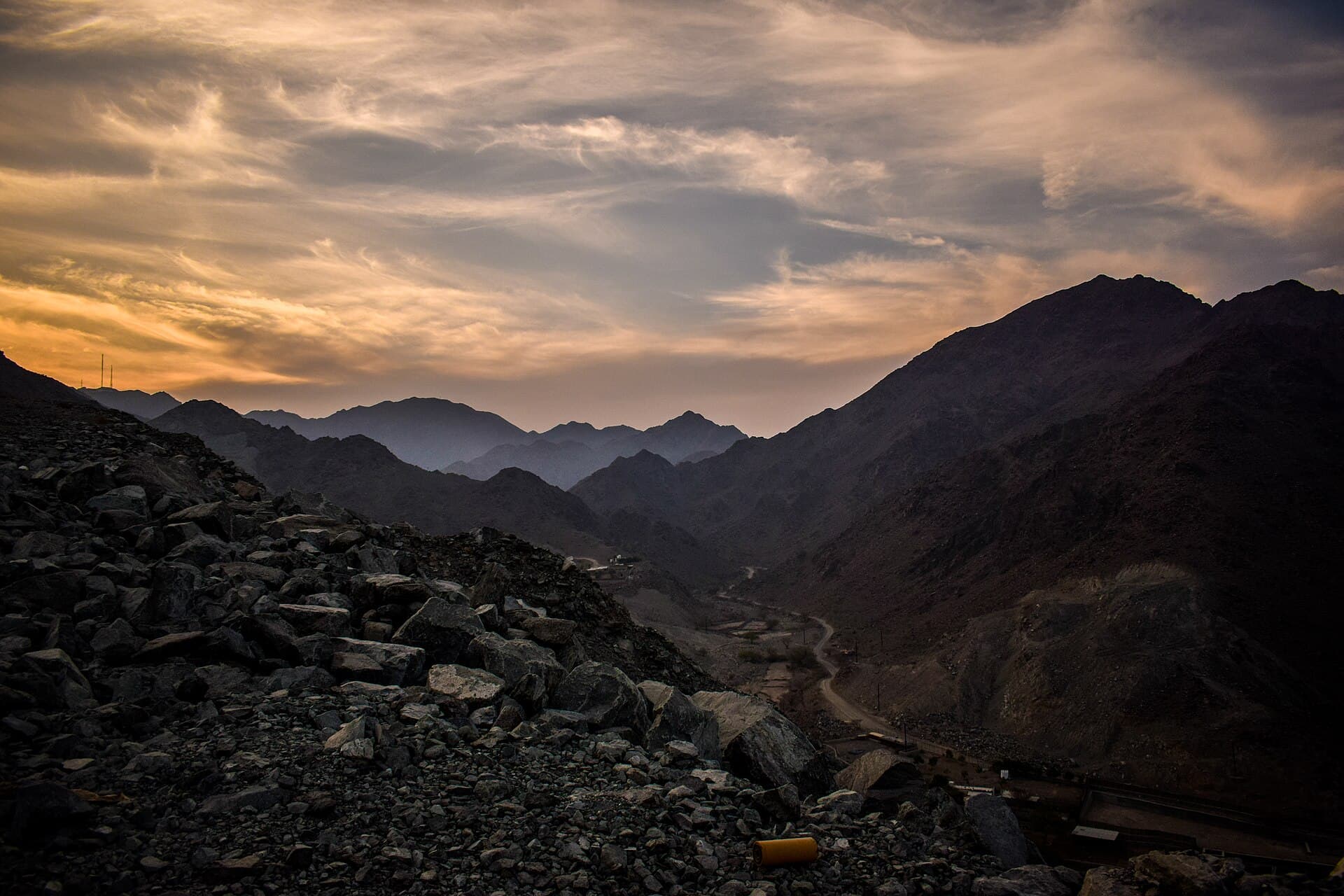 The rocky peaks of the Hajar Mountains silhouetted at dusk above a winding road near Fujairah