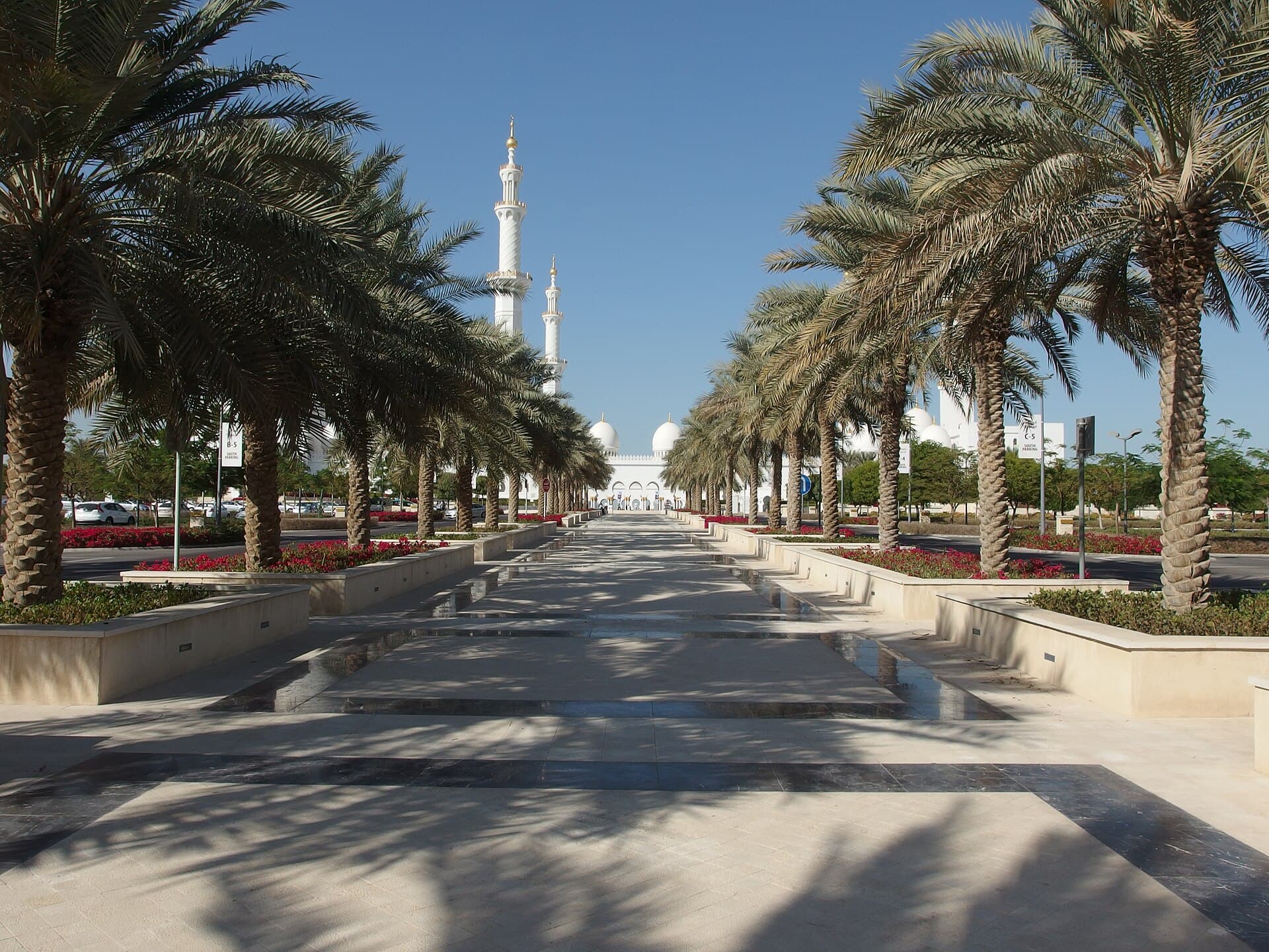 Sheikh Zayed Grand Mosque's white minarets and domes framed by a palm-lined marble approach under a clear sky