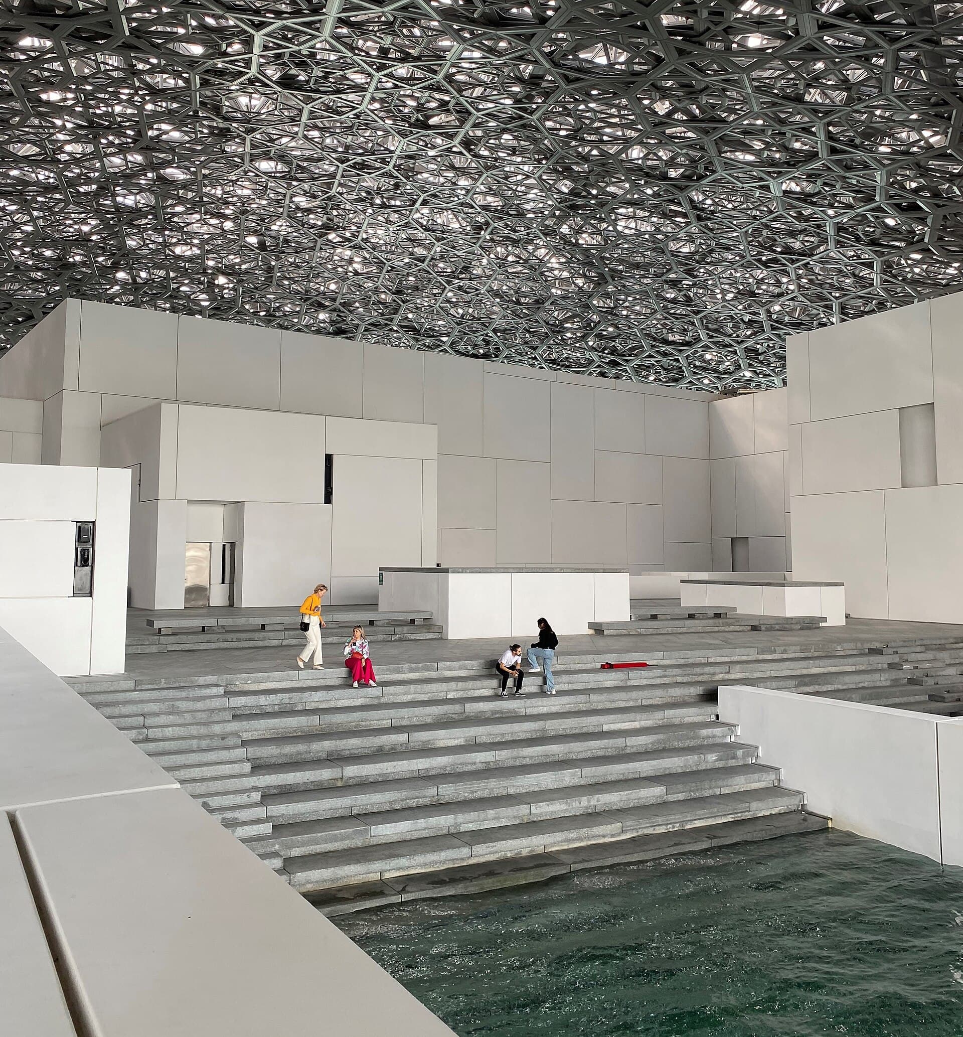 The Louvre Abu Dhabi's perforated dome scattering a rain of light across the museum's stepped courtyard
