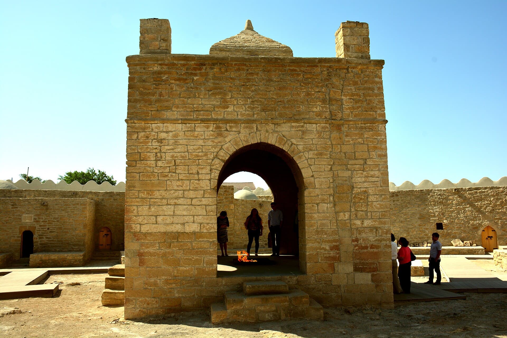 The central fire pit of Ateshgah Fire Temple, framed by a stone archway with visitors gathered around
