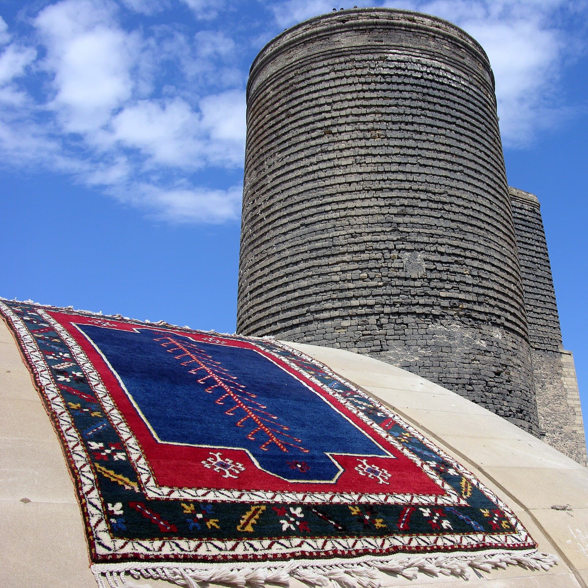 The stout stone cylinder of the Maiden Tower rising above Icherisheher's old city walls under a blue sky