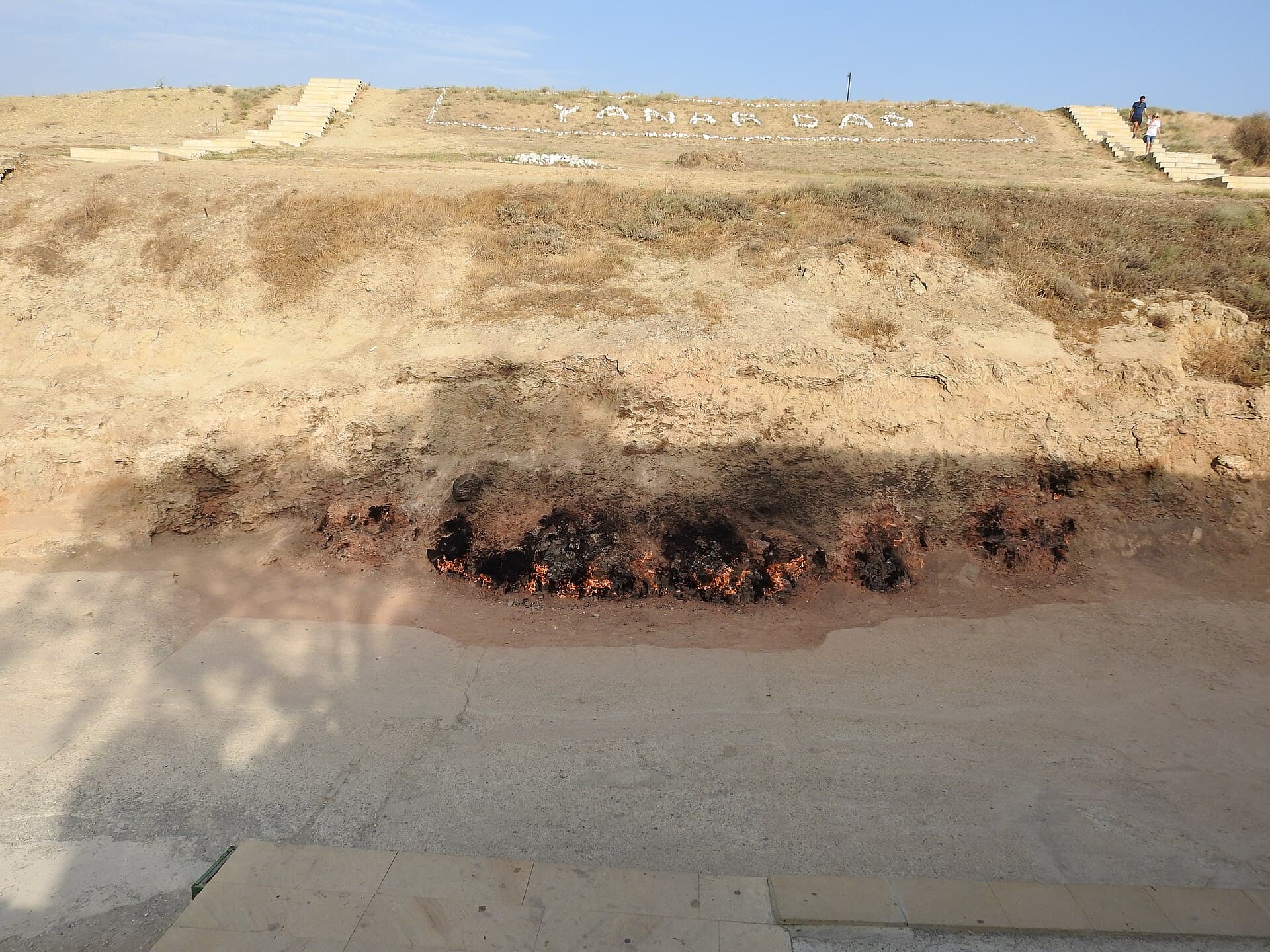 Flames burning continuously along the base of the Yanar Dag hillside, its name spelled out in white stones above