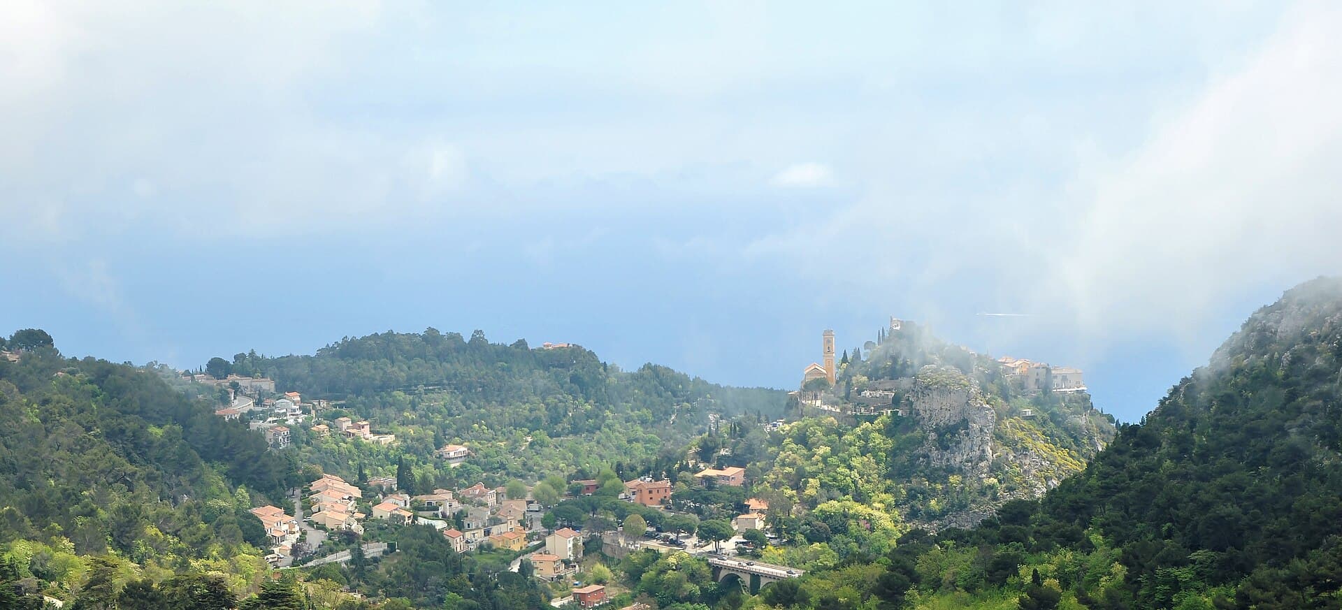 The medieval village of Èze perched on its rocky pinnacle above the Riviera coastline, hazy sea and hills behind