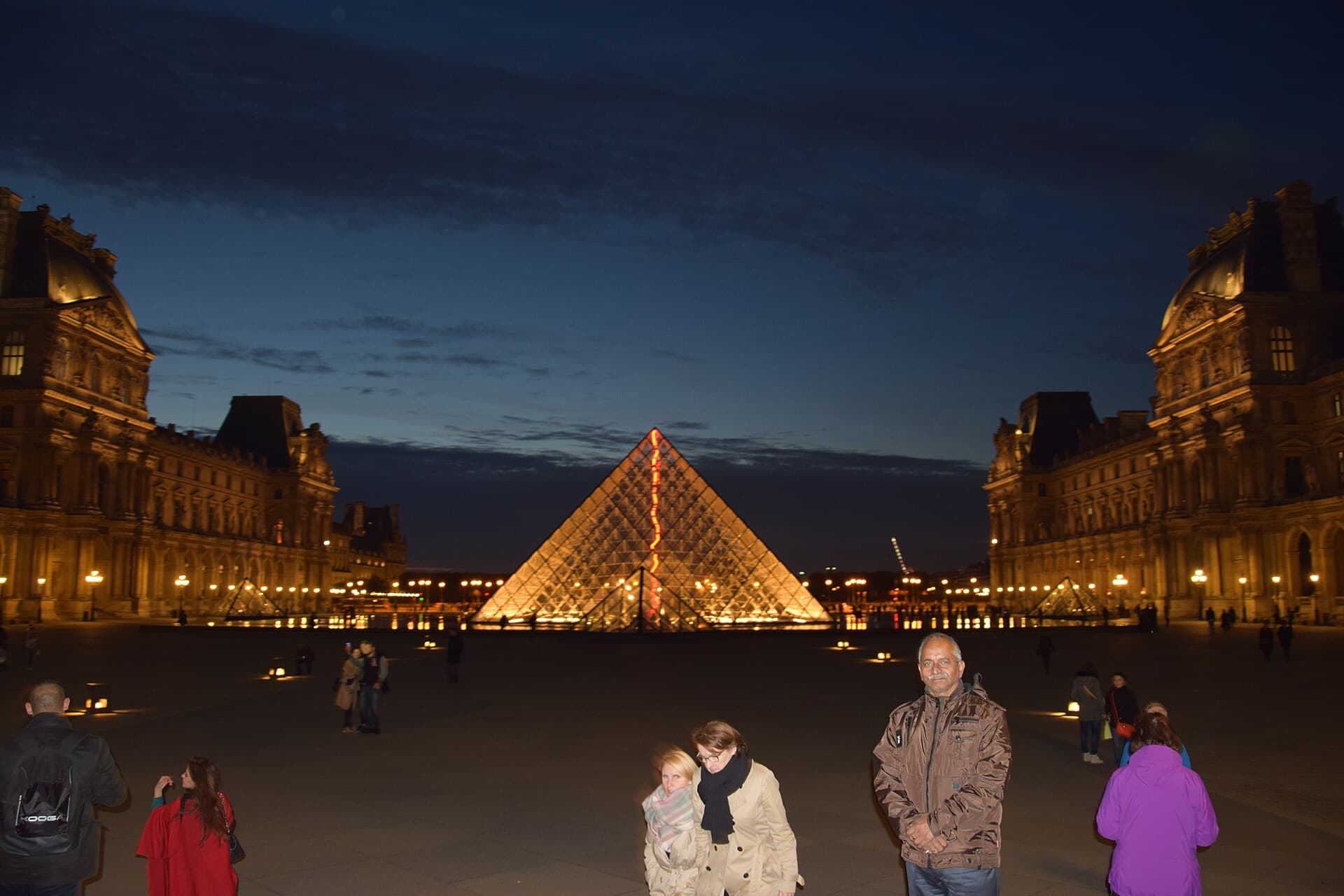 The Louvre's glass pyramid glowing gold at dusk, flanked by the palace's ornate stone wings