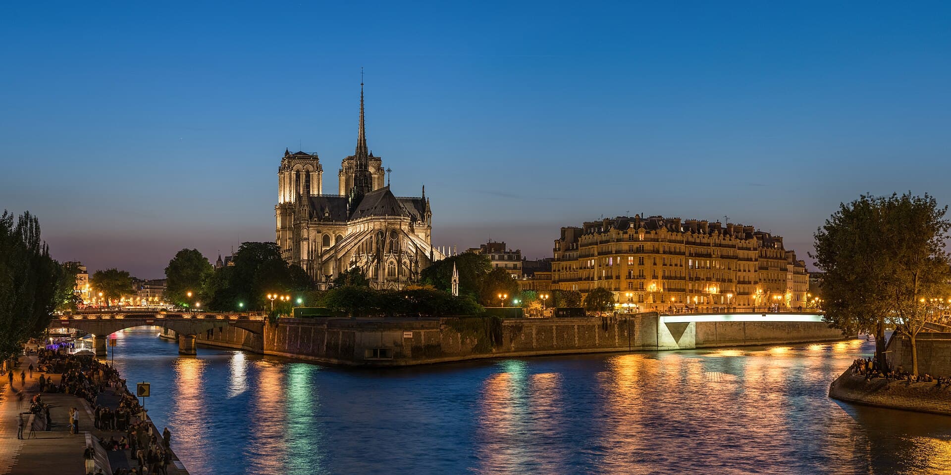 Notre-Dame's towers and spire lit up at dusk on the Île de la Cité, reflected in the Seine