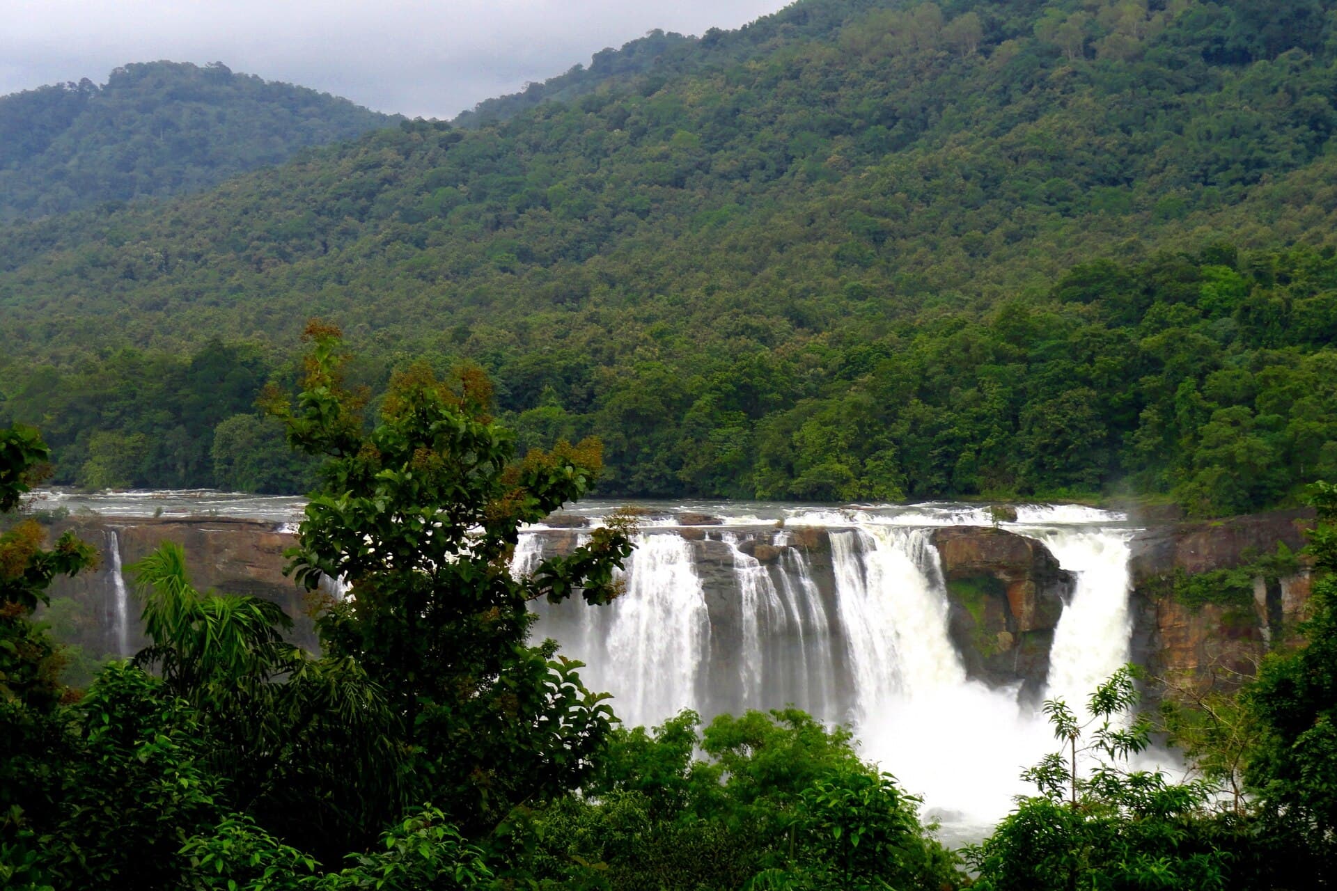 The wide white curtain of Athirappilly Falls dropping off a forested plateau in full monsoon flow