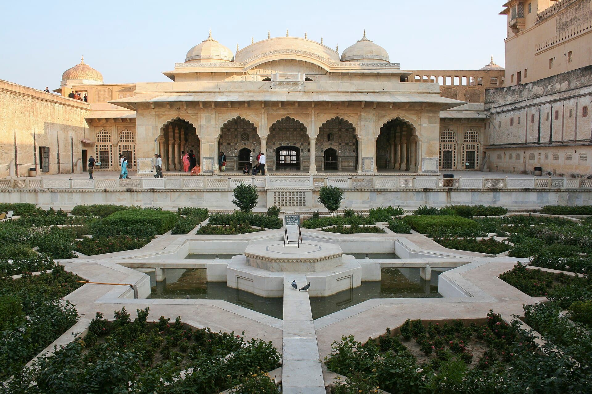 The Sheesh Mahal pavilion at Amber Fort behind its star-shaped charbagh garden, marble arches glowing in evening light