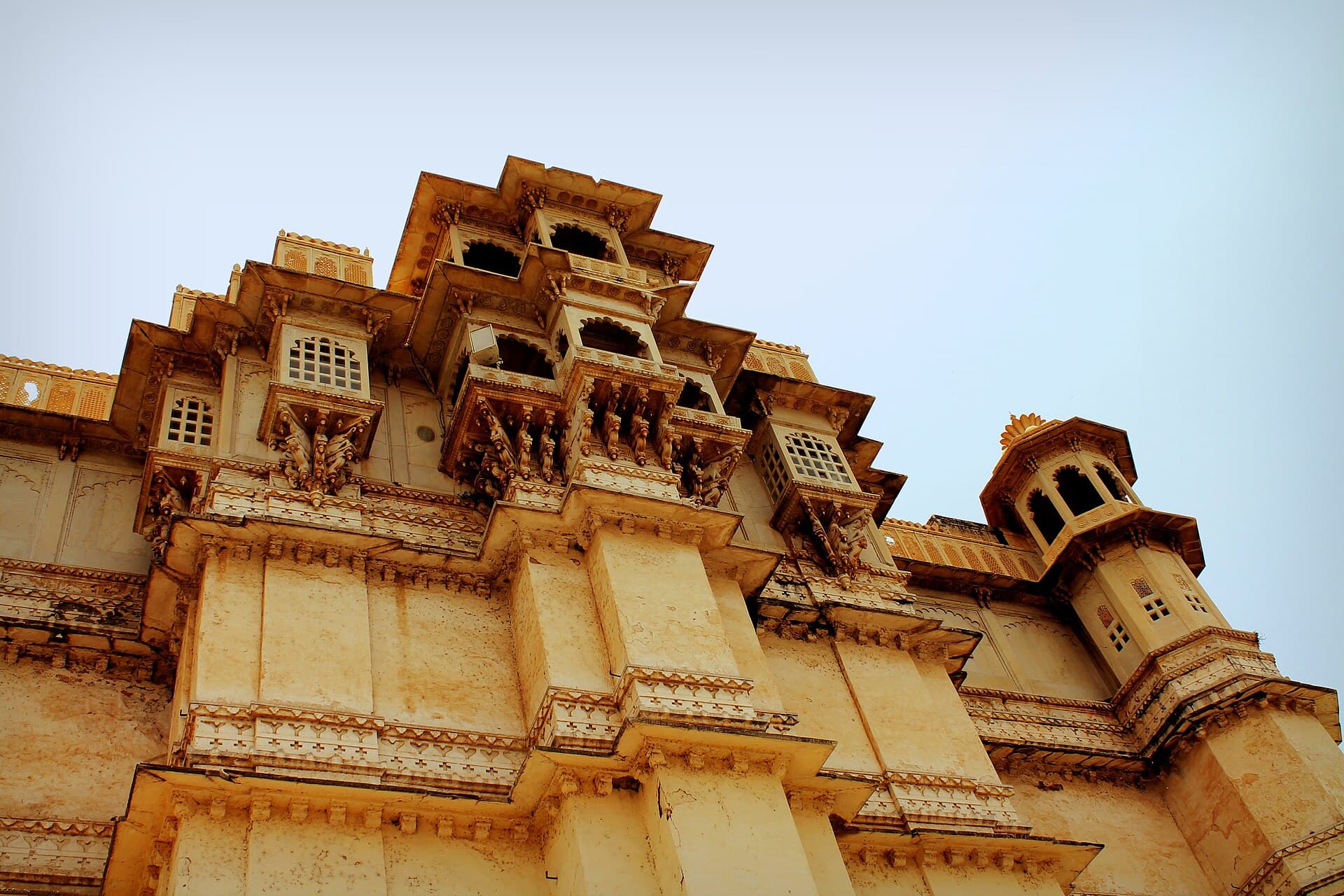 Looking up at the carved jharokha balconies and corner turrets of Udaipur's City Palace in golden stone