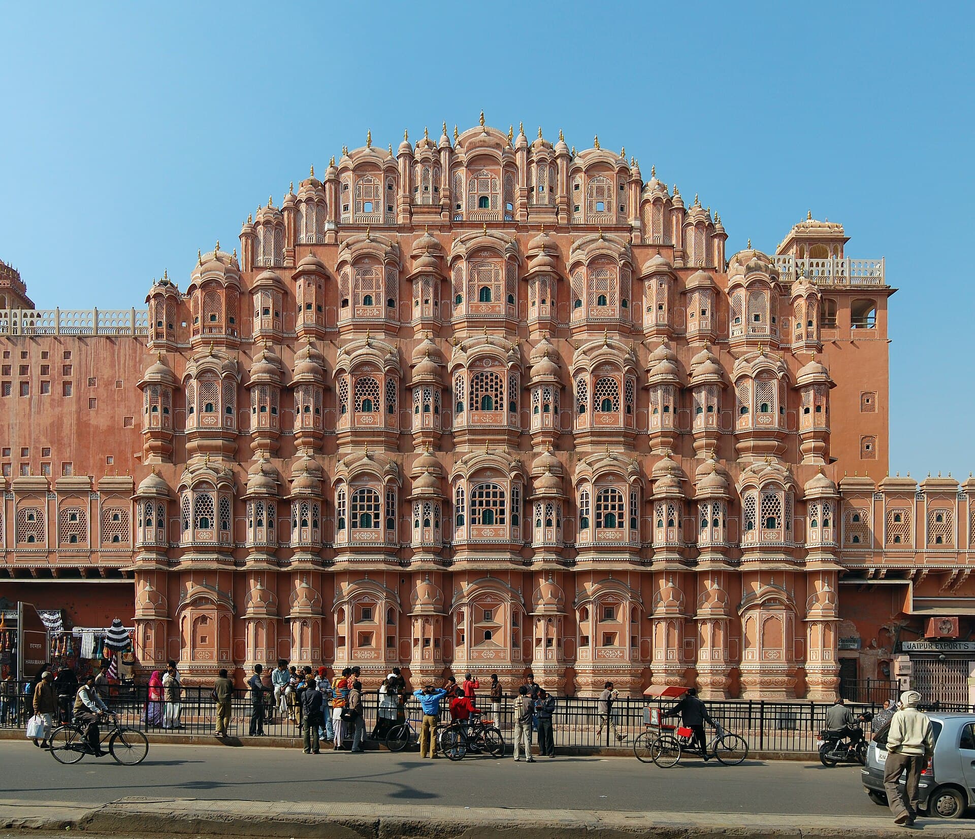 The full pink five-storey honeycomb facade of Hawa Mahal with its 953 jharokha windows, street life passing below