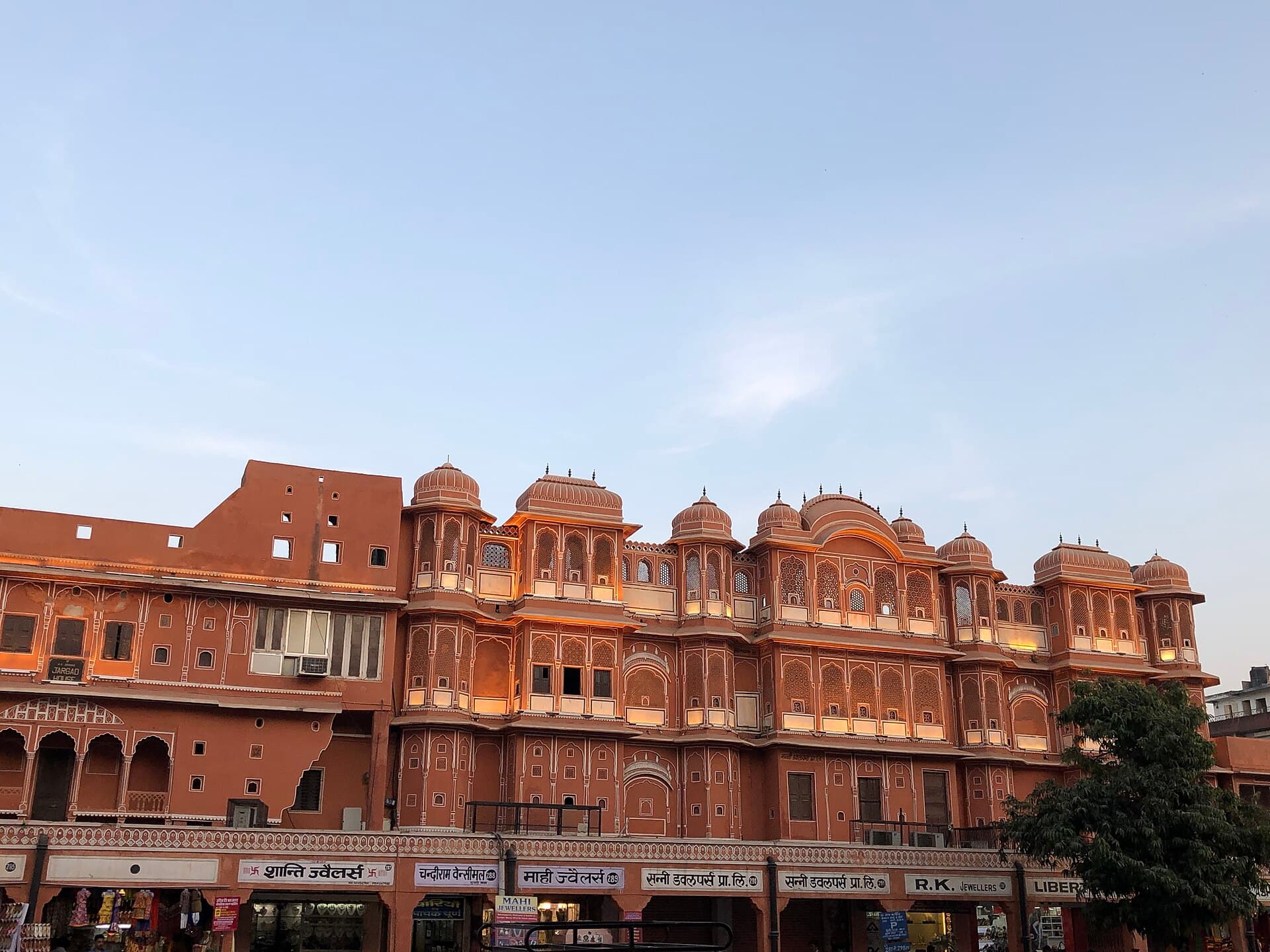 Pink-washed heritage facades with domed chhatris above a row of jewellers' shopfronts in Jaipur's walled old city at dusk
