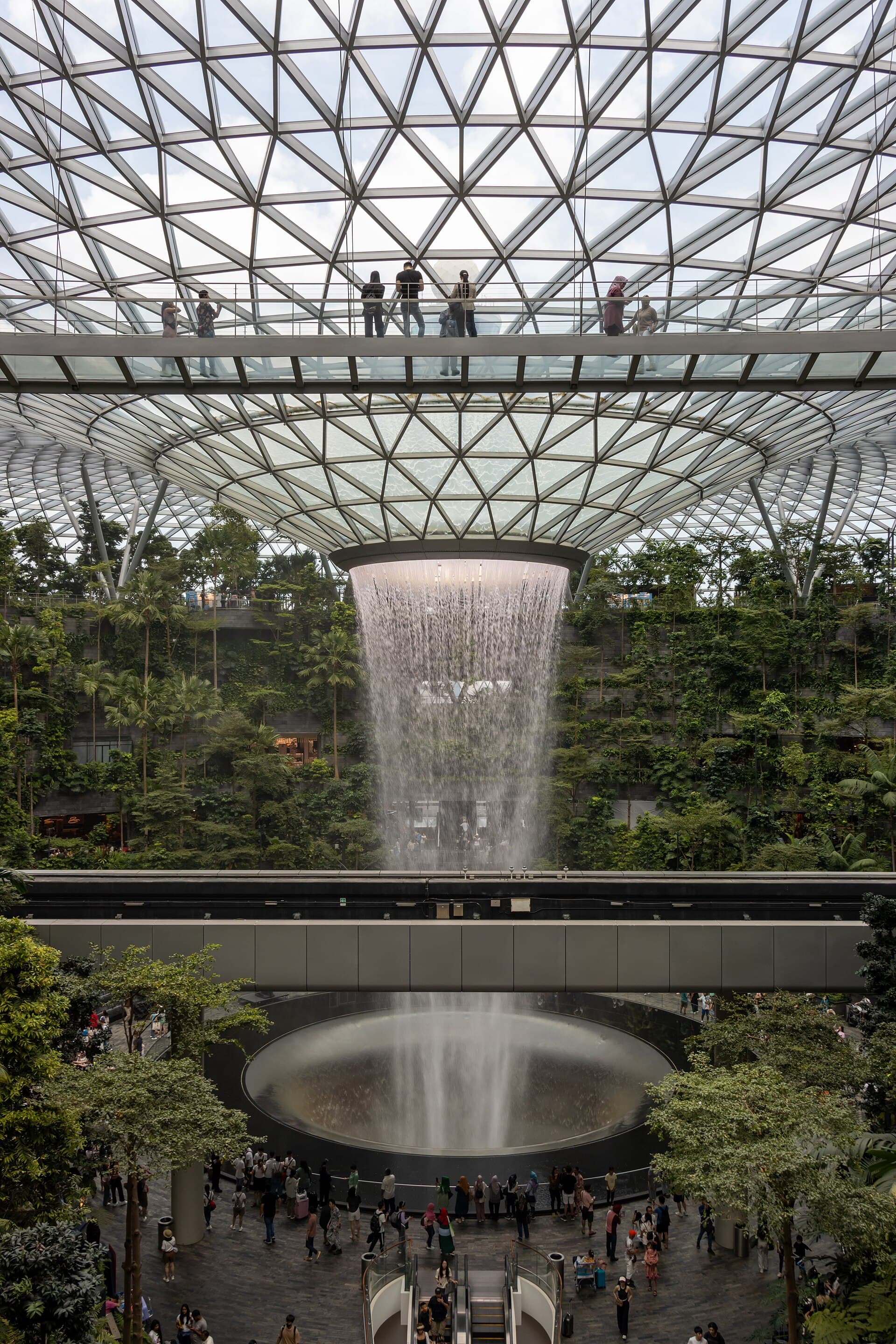 The Rain Vortex pouring through the centre of Jewel Changi's latticed glass dome into a planted forest valley below